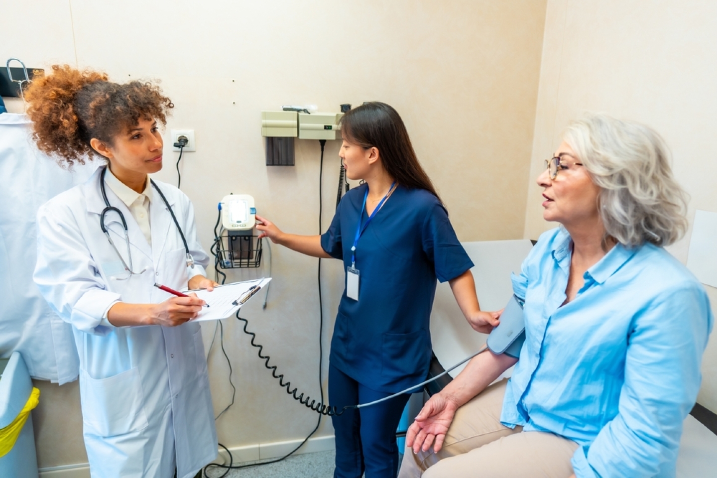 Medical professionals taking care of elderly woman's health, performing blood pressure check in hospital room