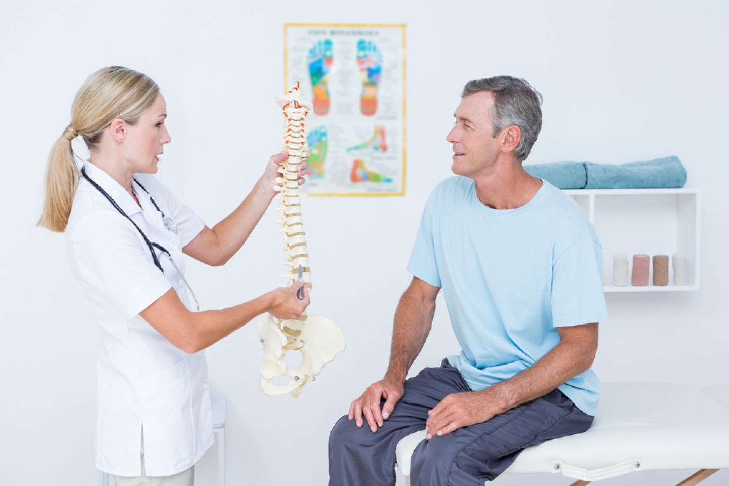Doctor showing anatomical spine to her patient in medical office.