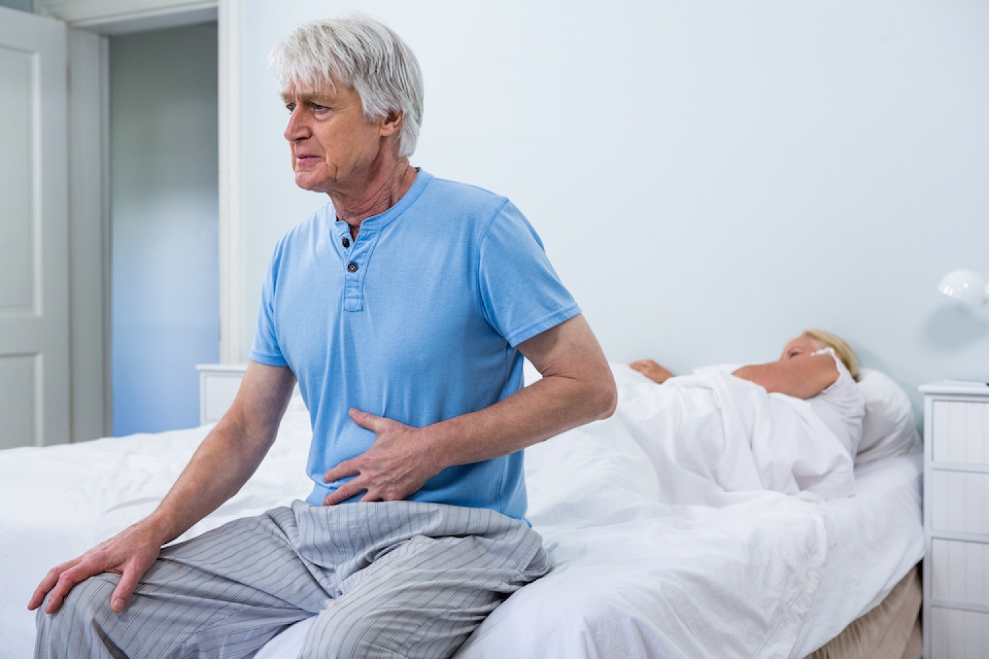 older man sits upright due to pain