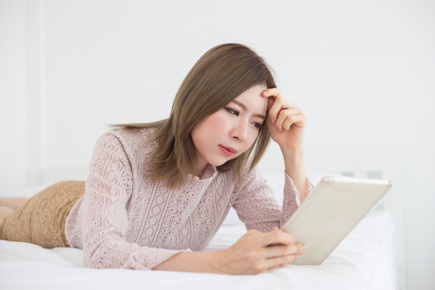 Asian woman looking in tablet on bed