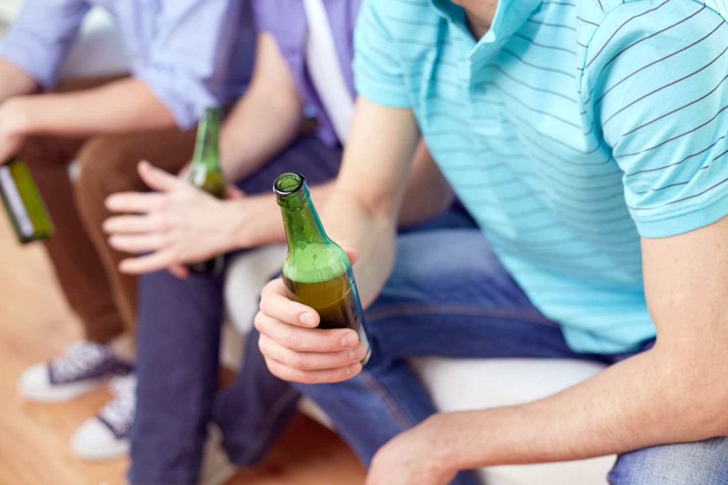 men with beer bottles sitting on sofa at home