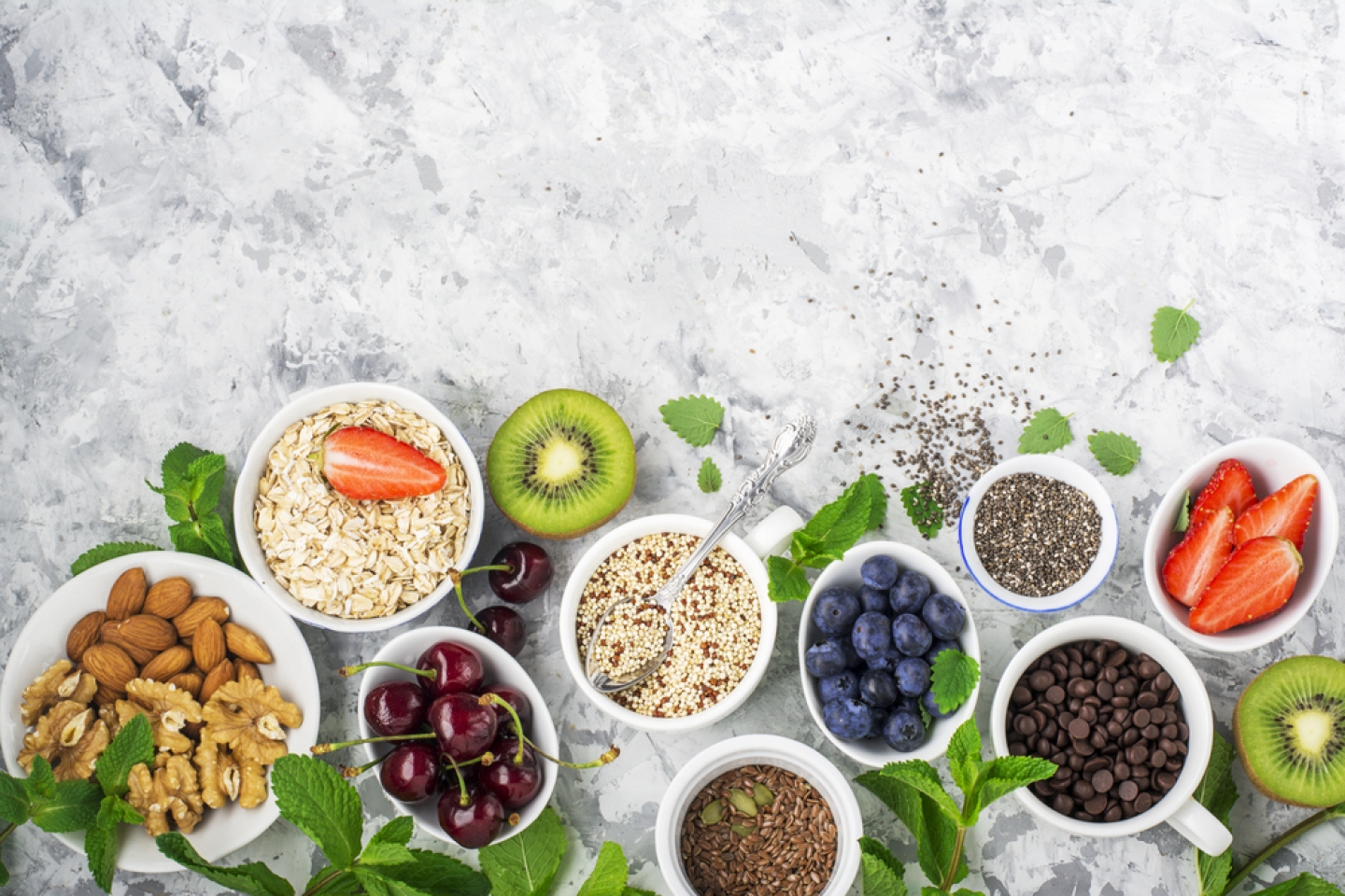 Healthy fitness food from fresh fruits, berries, greens, super food: kinoa, chia seeds, flax seed, strawberry, blueberry, kiwi, cherry, almonds, walnuts, mint, oatmeall flakes on a light background.