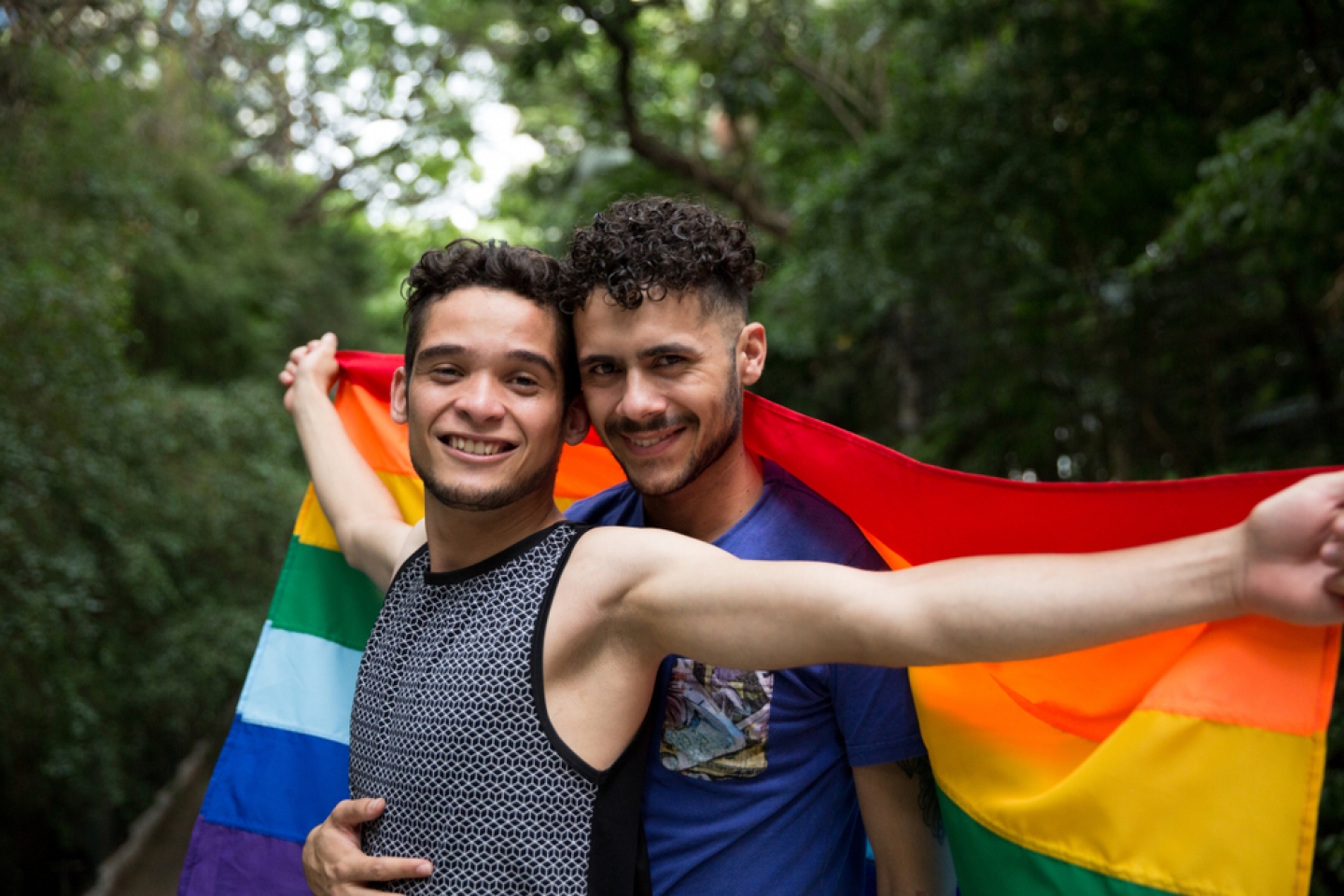 Gay Couple Embracing with Rainbow Flag in the Park