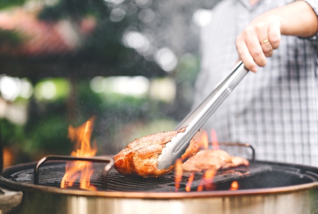 Man hand holding tongs grilling barbecue on fire at backyard on day.