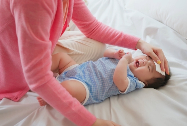 authentic shot of asian baby has fever and his mother checks body temperature by thermometer on bed