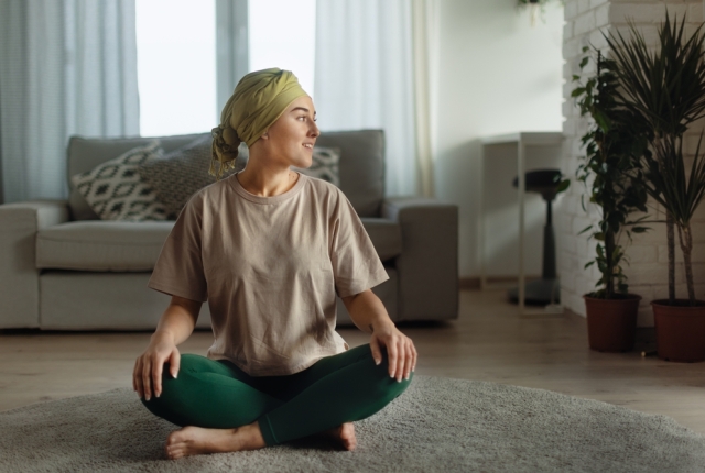 Young woman with cancer taking yoga and meditating in her apartment.