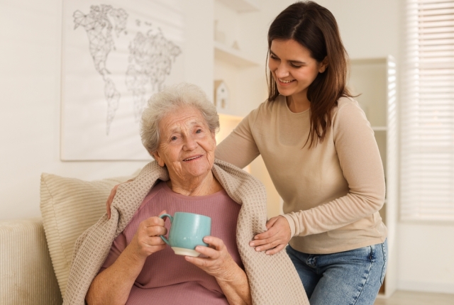 Granddaughter giving hot drink to her grandmother at home. Elderly care