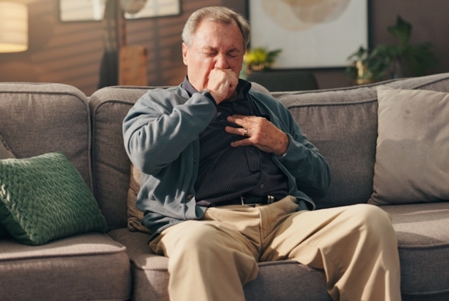Senior, sick man and couch with chest pain on sofa for cardiac arrest or bronchitis at home. Elderly, male person or patient with illness, virus or viral infection for lung disease or heart attack
