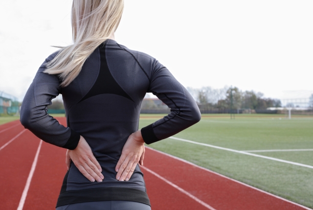 Athletic fitness woman rubbing the muscles of her lower back. Sports exercising injury.