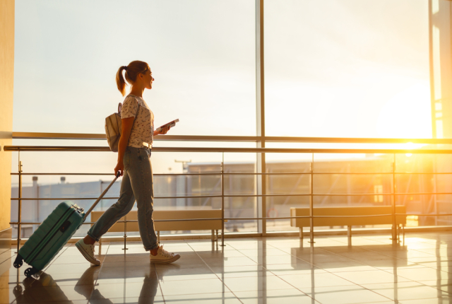 young woman goes at airport at window with a suitcase waiting for plan