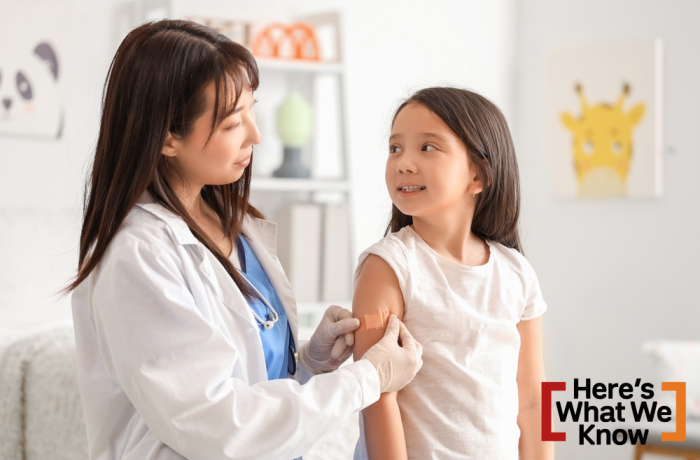 Female Asian doctor applying medical patch on little girl's arm after vaccination in clinic
