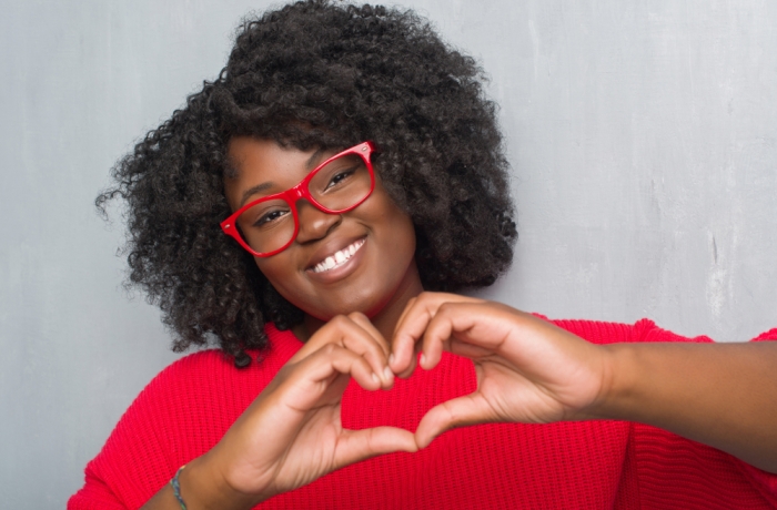 Young african american plus size woman over grey grunge wall wearing winter sweater smiling in love showing heart symbol and shape with hands.