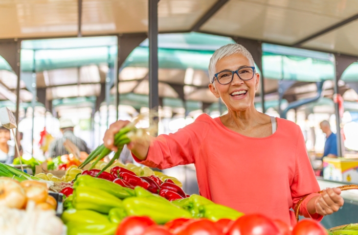 Beautiful senior woman buying vegetables at a farmers market. Woman on greenmarket. Senior woman picking fresh produce at the market. Farmers Market Shopping Mature Woman