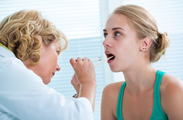 Doctor checking with depressor sore throat to teenage girl 