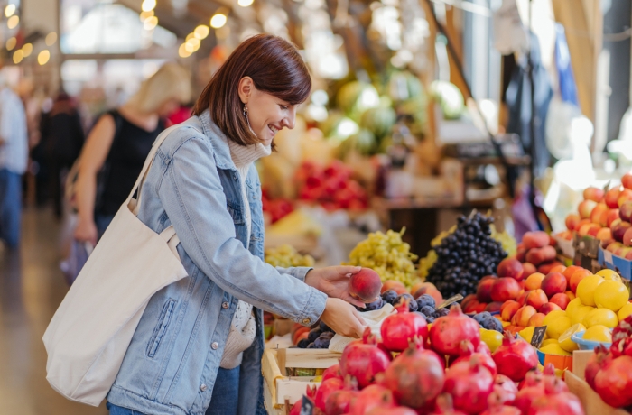 Woman is chooses fruits and vegetables at food market. Reusable eco bag for shopping. Sustainable lifestyle. Eco friendly concept. 