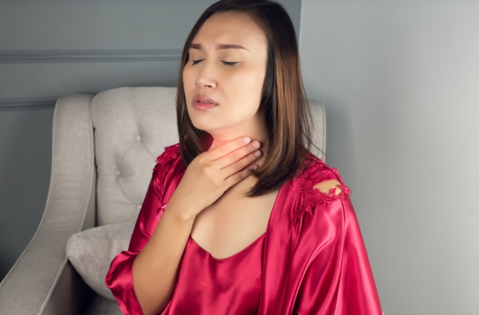  A woman wearing a satin nightgown and red robe suffering from hoarseness or laryngitis in the living room at night.
