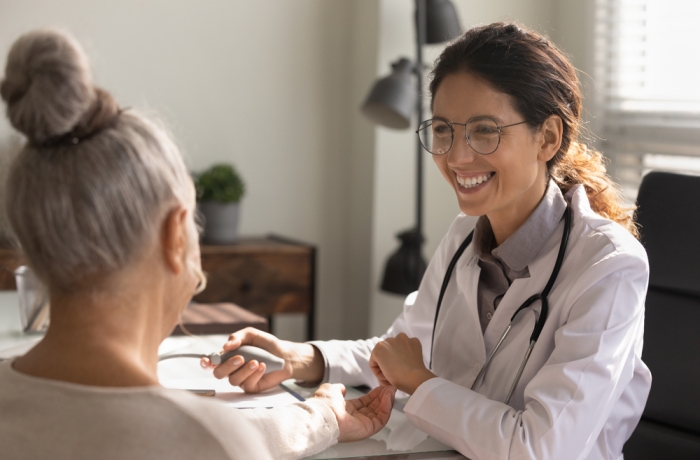 Close up smiling female doctor wearing glasses checking old woman blood pressure at meeting in hospital office,