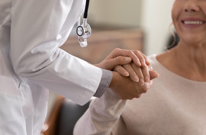 Close up shot of young female physician leaning forward to smiling elderly lady patient holding her hand in palms.