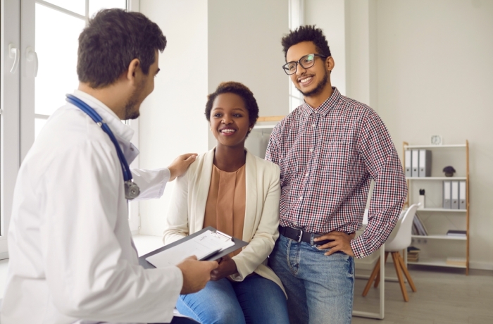 Male doctor comfort support multiracial couple patients at consultation in clinic. Man gynecologist caress show help understanding to ethnic family at hospital appointment. Good medicine concept.