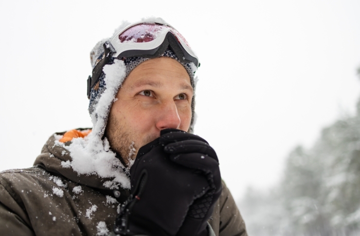 An adult brutal man with a beard in a winter forest all face in the snow. Man shivering in cold winter and rubbing hands until snow.