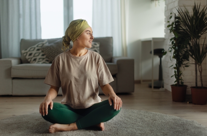 Young woman with cancer taking yoga and meditating in her apartment.