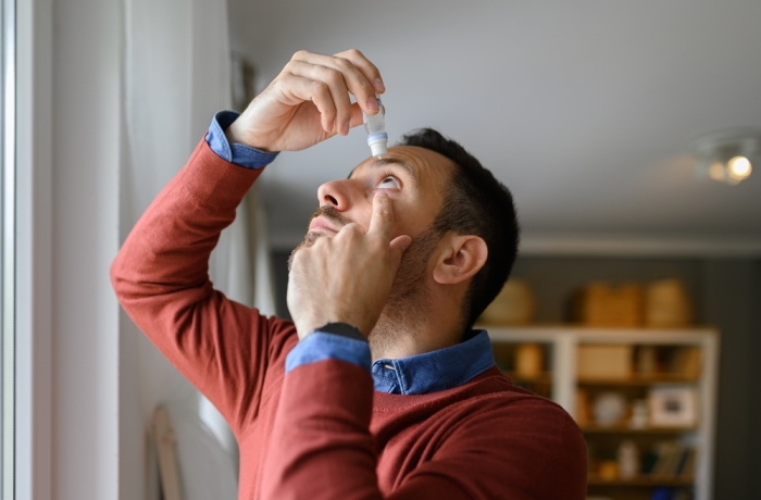 Close-up of young man applying eye drops to treat dry eye and irritation at home