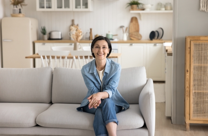 Attractive middle-aged woman housewife in casual clothes relaxing sit on sofa at home, smile look at camera feel satisfied with calm, well-being retired life. Portrait of happy homeowner or tenant