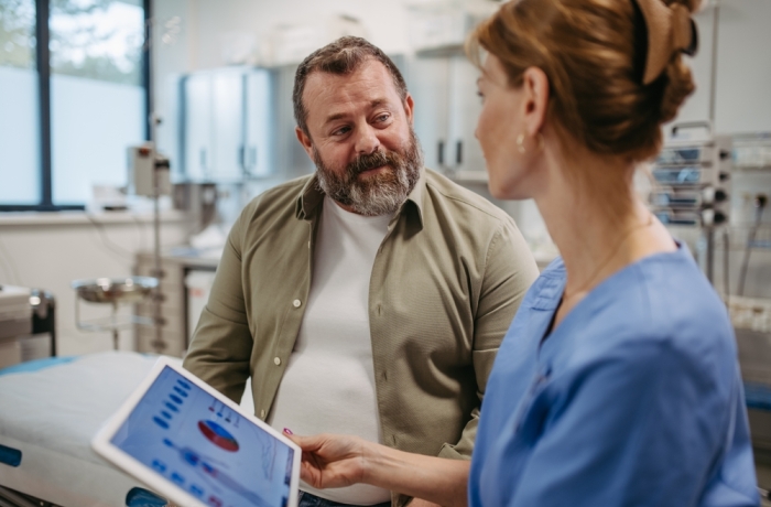 Female doctor consulting with overweight patient, discussing test result in doctor office. Obesity affecting middle-aged men's health. Concept of health risks of overwight and obesity.