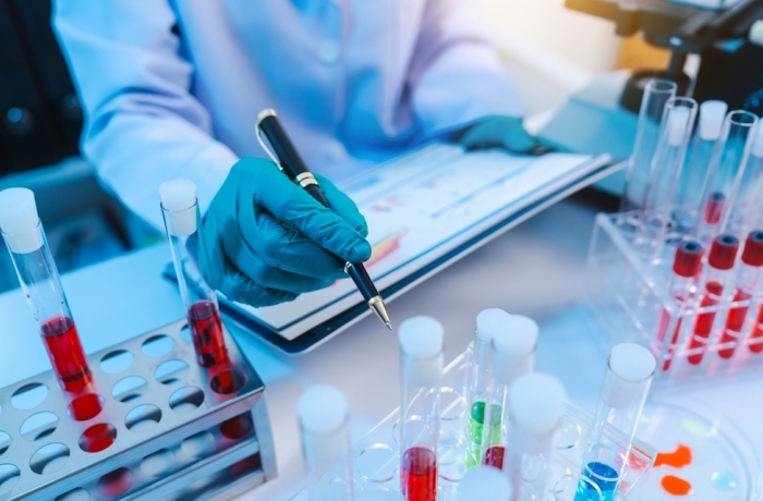 Asian people scientist in lab coat and protective gloves working with test tubes with green and red liquids, with microscope and other test tubes in the background in laboratory.