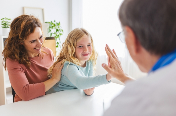 Senior male doctor give high five to little cute girl at medical consultation. Cute kid visiting hospital with her mother. Children healthcare concept.