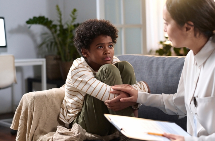 Portrait of young African American boy listening to caring psychologist in therapy session for children