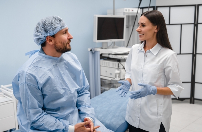 A young female doctor gastroenterologist consults talks to male patient man in a modern medical private clinic cabinet before gastroduodenoscopy procedure. Gastroscopy endoscopy concept