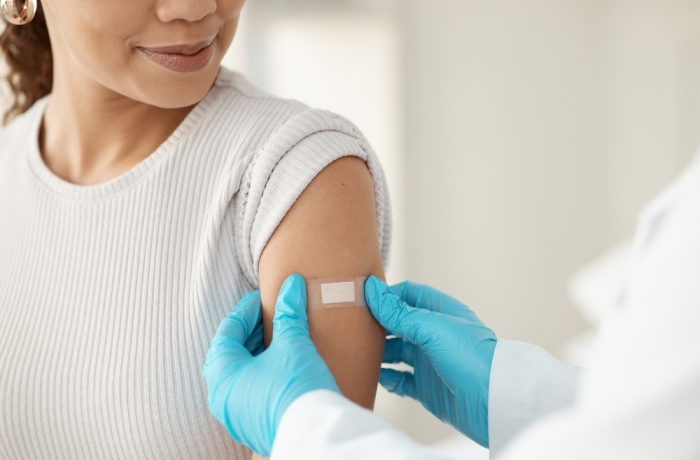 Vaccine, happy woman and hands of doctor with plaster for health, wellness and service in clinic.