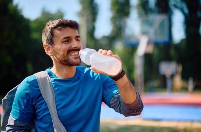 Happy athletic man drinking water after sports training outdoors. 