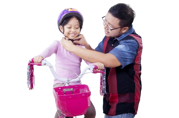 Young dad teach his daughter to ride a bike and fasten helmet on the daughter's head, isolated on white