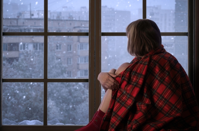 Girl sits on the window sill of the window and looks at the falling snow. The concept of home comfort, season, solitude