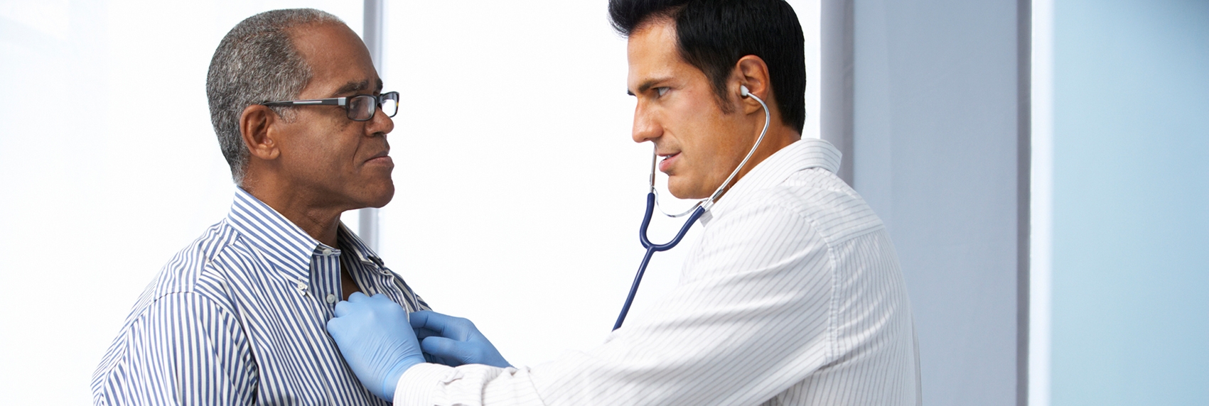 Male doctor listening to older patient's heart using a stethoscope.