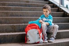 Sad young boy sitting on steps with backpack