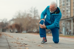 The senior man use hands hold on his knee while running outdoor