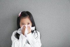 young girl sneezing into a tissue