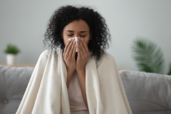 sick woman blowing her nose under the blanket