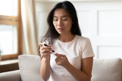 Young Asian diabetes patient woman sit on couch pinch finger measure blood sugar level at home.