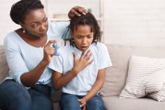 Preventing Attack. Black woman giving blue asthma inhaler to her sick breathless child at home, free space