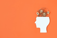 Silhouette of human head and wooden blocks with the letters ADHD on orange background.