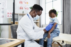 Male physician using syringe for vaccinating little girl from coronavirus at modern hospital.