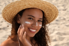 Beautiful African American woman with sun protection cream on face at sandy beach