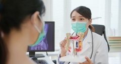 asian woman wears face mask to prevent COVID19 has colorectal cancer diagnosis in hospital - female doctor showing colonoscopy results and xray to patient on computer and explain by anatomical model