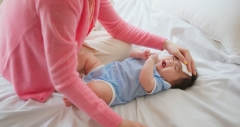 authentic shot of asian baby has fever and his mother checks body temperature by thermometer on bed