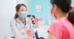 asian female doctor wear white coat and face mask explaining uterus model to woman in hospital