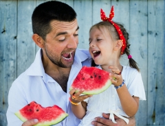 happy father playing with cute little daughter holding watermelon